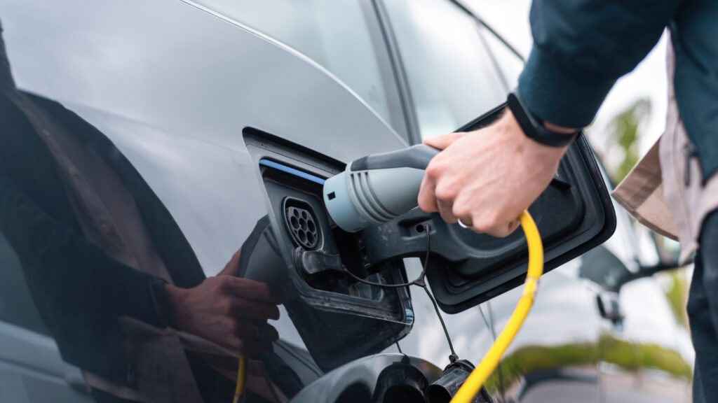 Hombre con enchufe de carga en auto electrico. Tipos de combustibles