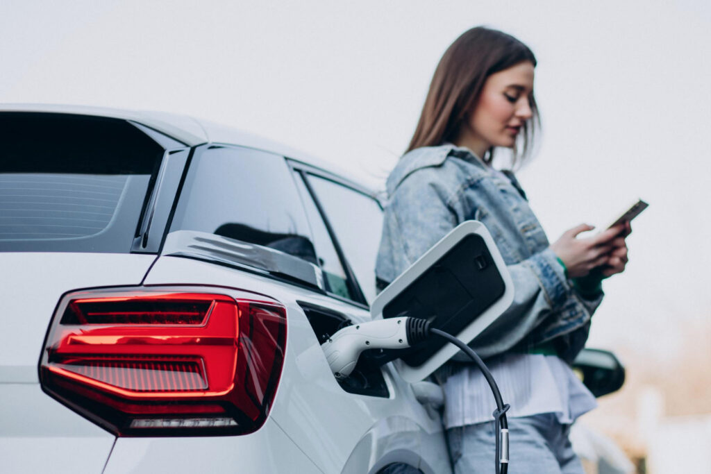 mujere cargando su auto híbrido mientras espera con celular